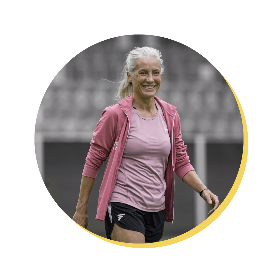 Woman in athletic wear smiling while walking on a sports field.